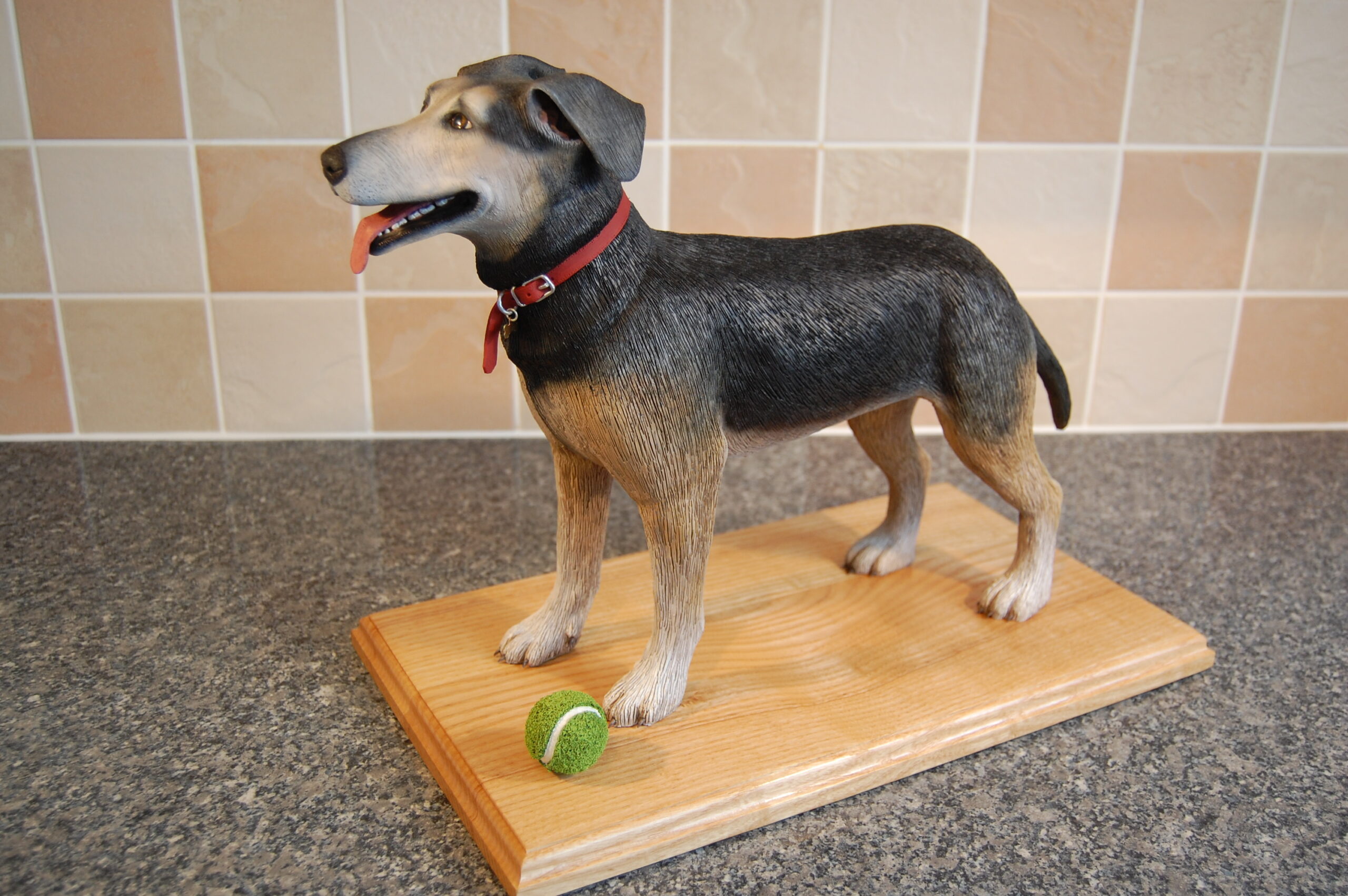 Sculpture of a black, white and tan dog, standing with a tennis ball at his front feet.